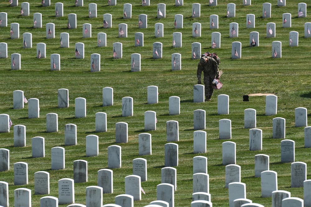A service member places a flag during the annual Flags-In ceremony at Arlington National Cemetery on May 27, 2021. (Matt McClain/The Washington Post)